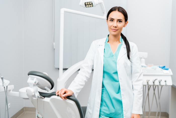 attractive dentist standing near chair in dental clinic