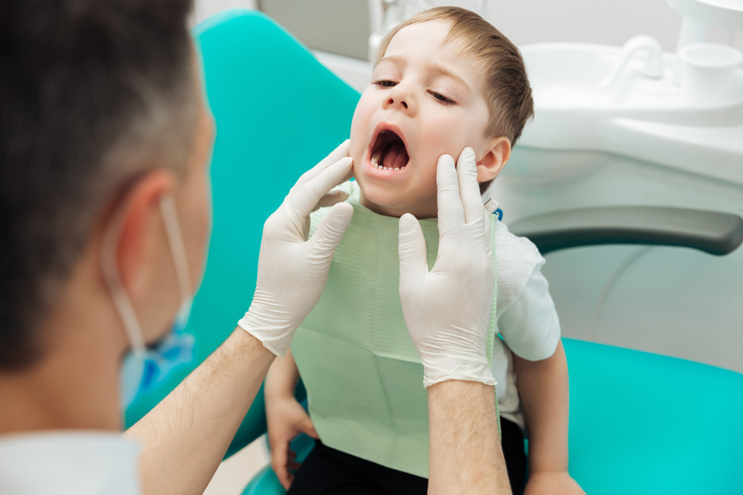 Dentist examining teeth of little boy witting with mouth opened