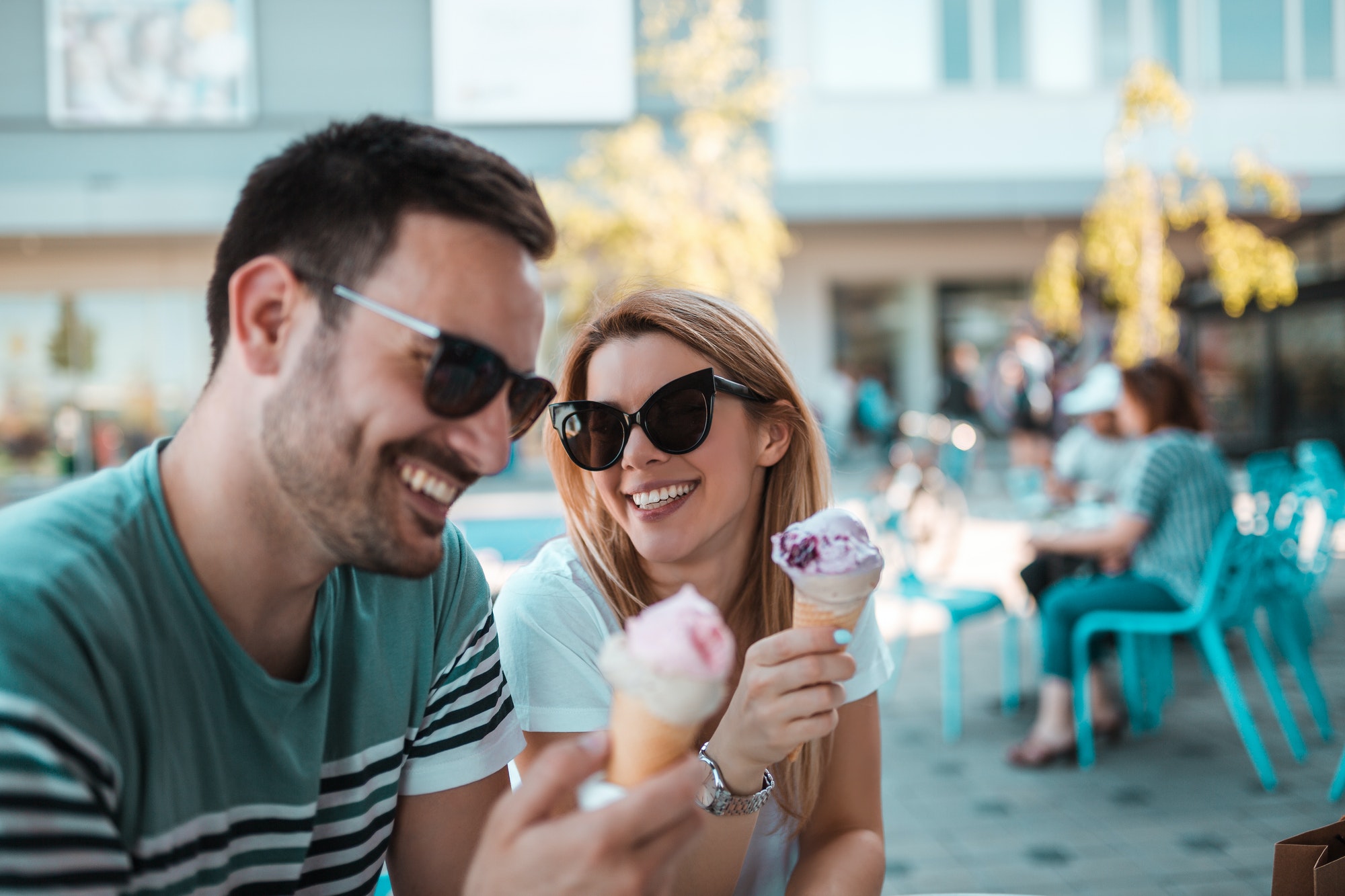 A beautiful young couple with sunglasses are sitting outdoors and having ice-creams in cornet