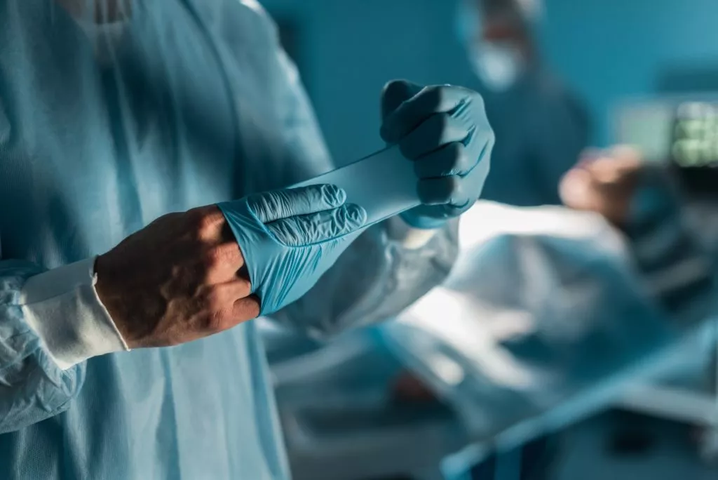 cropped image of surgeon taking off medical gloves in surgery room