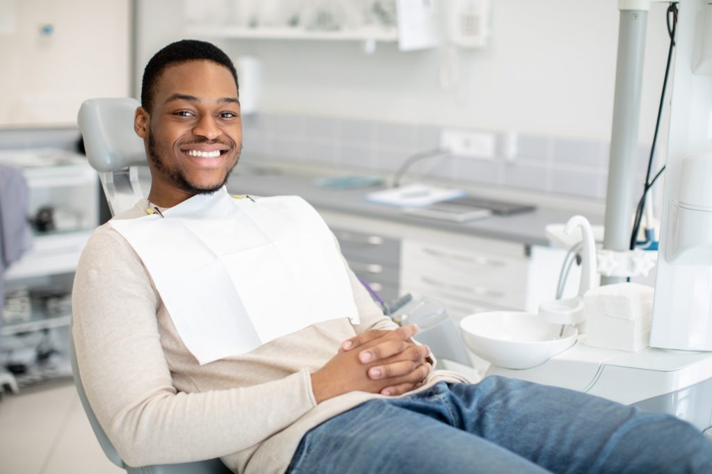 Dental Clinic. Joyful Young Black Guy Sitting In Chair Iin Stomatological Cabinet