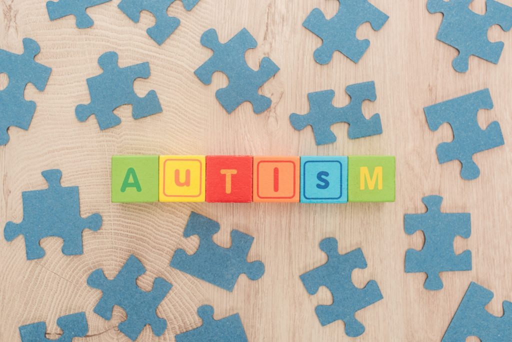 top view of autism lettering made of multicolored cubes among blue puzzle pieces on wooden table