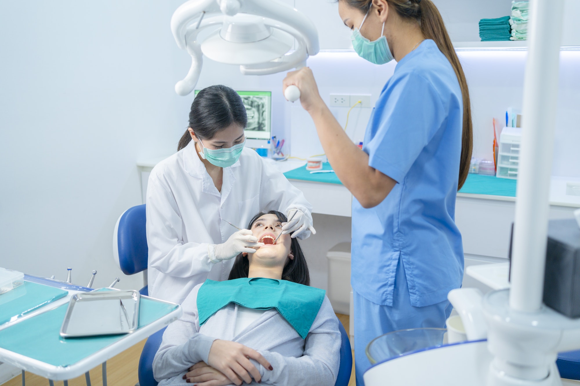 Asian dentist adjust dental surgical light then starts examining tooth patient at dental clinic