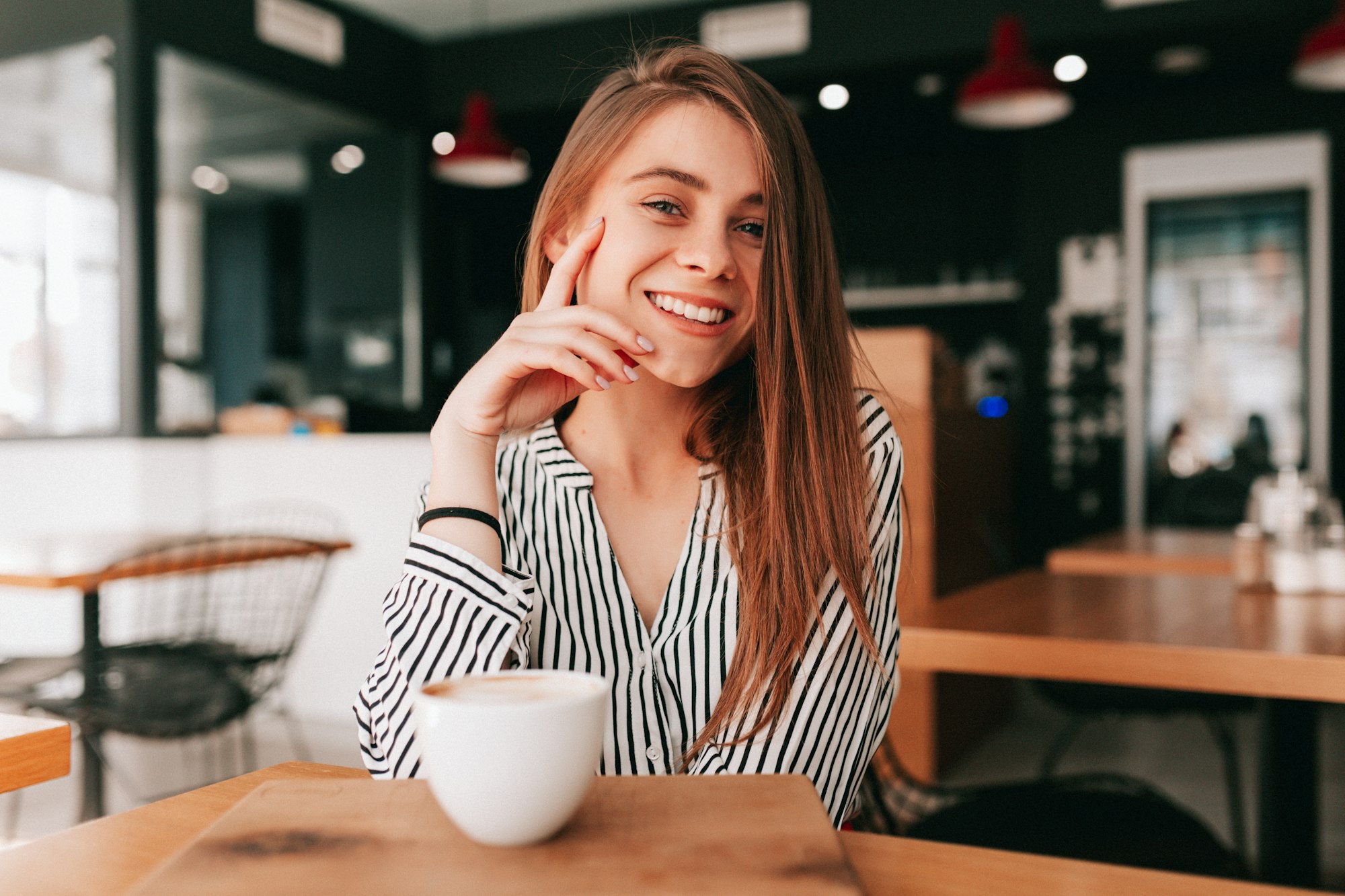 Adorable charming lady with long hair wearing trendy blouse sitting in cafeteria with great smile